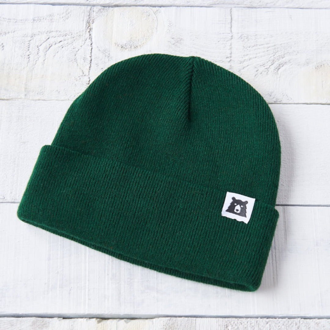 Green beanie with a logo on a white wooden surface