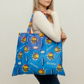 Woman holding a blue tote bag with cartoon bee design on a plain background