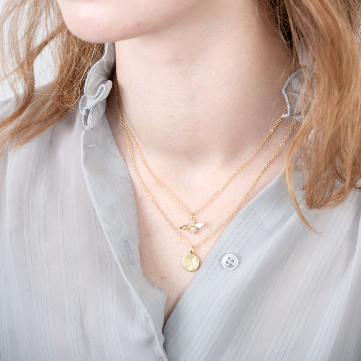 A pair of gold necklaces on a white card. The longer necklace features a honeycomb pendant, and the shorter necklace features a bee pendant. 