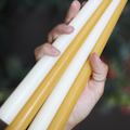 A hand holding three beeswax candles, one white and two yellow. The candles are long and thin.
