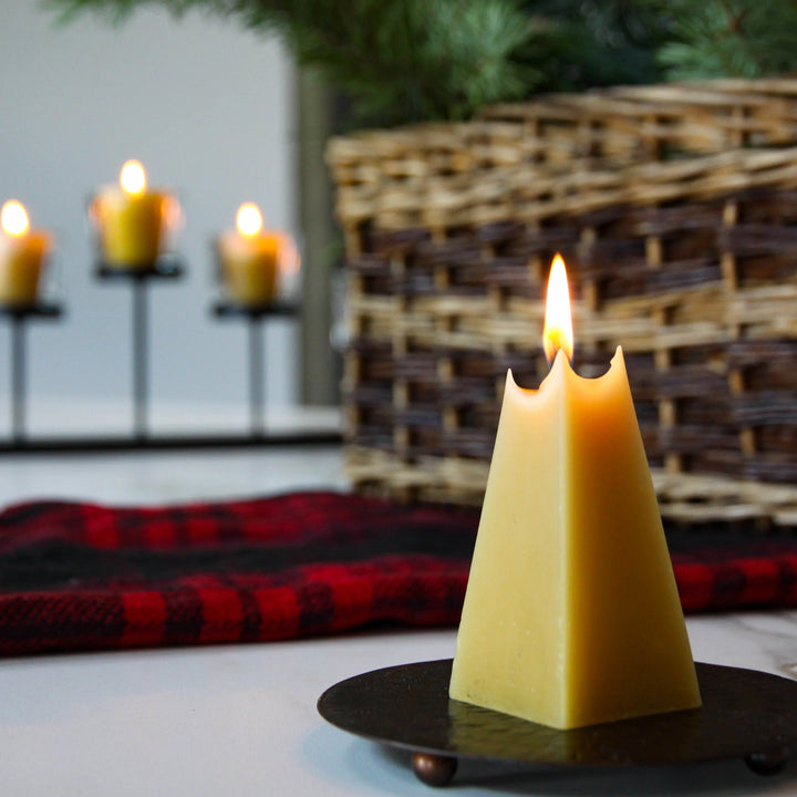 A yellow, pyramid-shaped beeswax candle. The candle has a smooth surface and a pointed tip. The base of the candle is slightly wider than the top.
