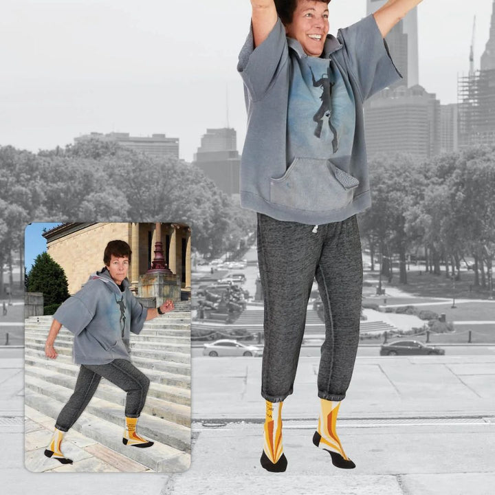 A pair of women's crew socks with a vibrant design of yellow and orange rays emanating from the bottom. Text on one sock reads 