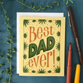 Greeting card with 'Best Dad Ever!' text on a blue background with pens and greenery.