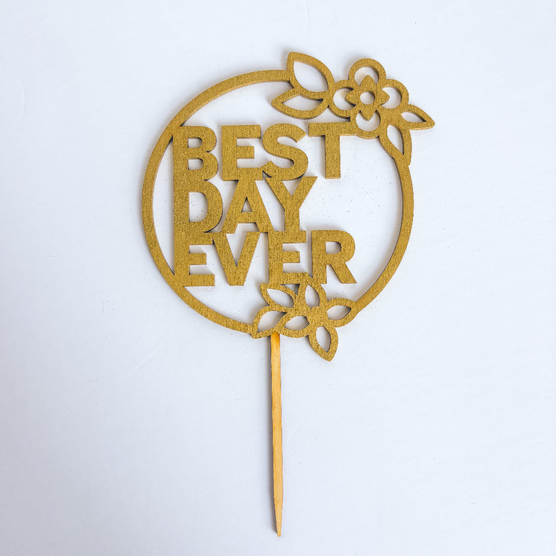 Gold 'Best Day Ever' cake topper on a white background