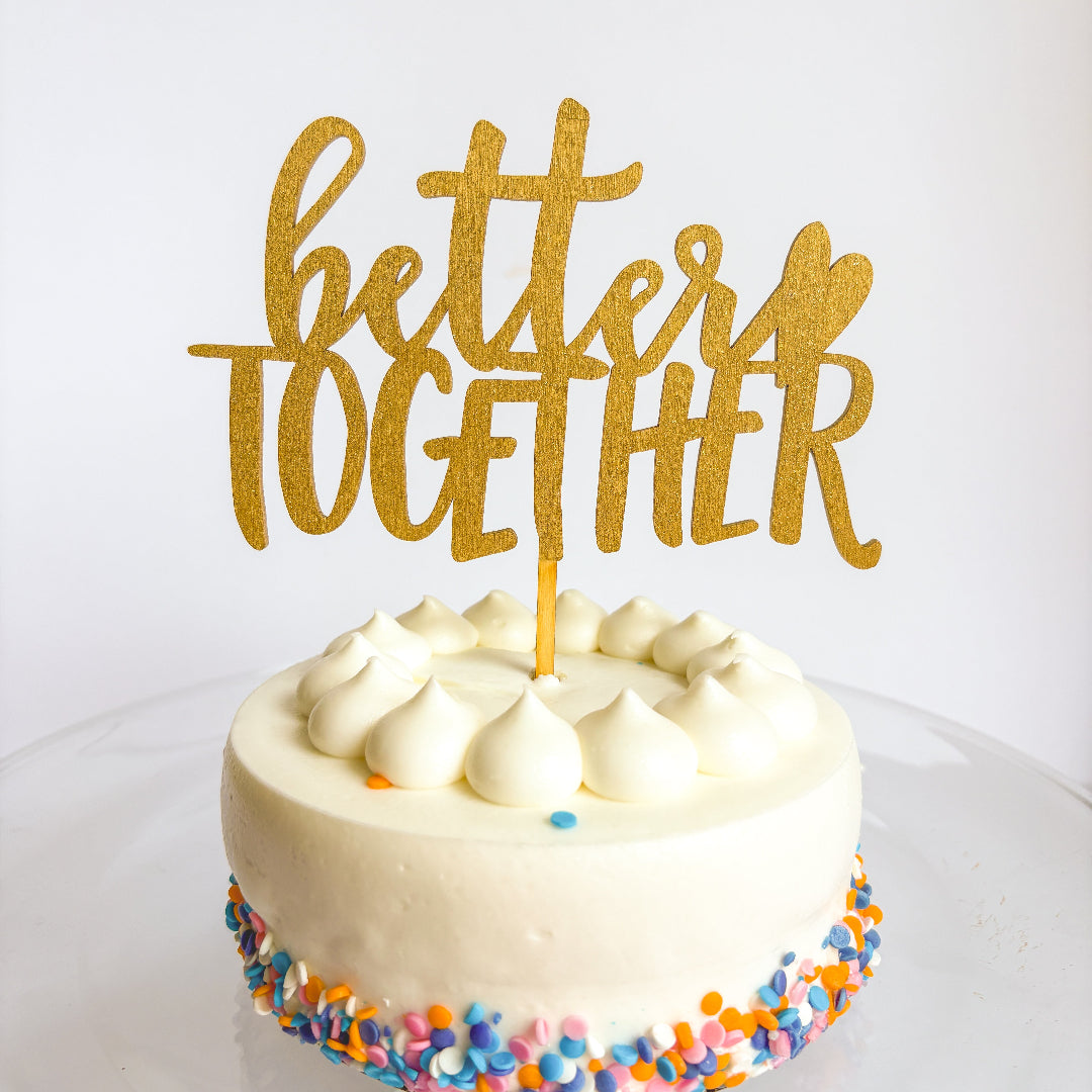 White cake with colorful sprinkles and a gold 'better together' topper on a white background