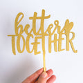 Gold glittery 'better together' sign held by a hand on a white background