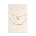 A pair of gold necklaces on a white card. The longer necklace features a branch pendant, and the shorter necklace features a bird pendant. 