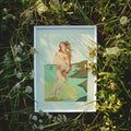 Framed artwork of a woman in nature surrounded by greenery