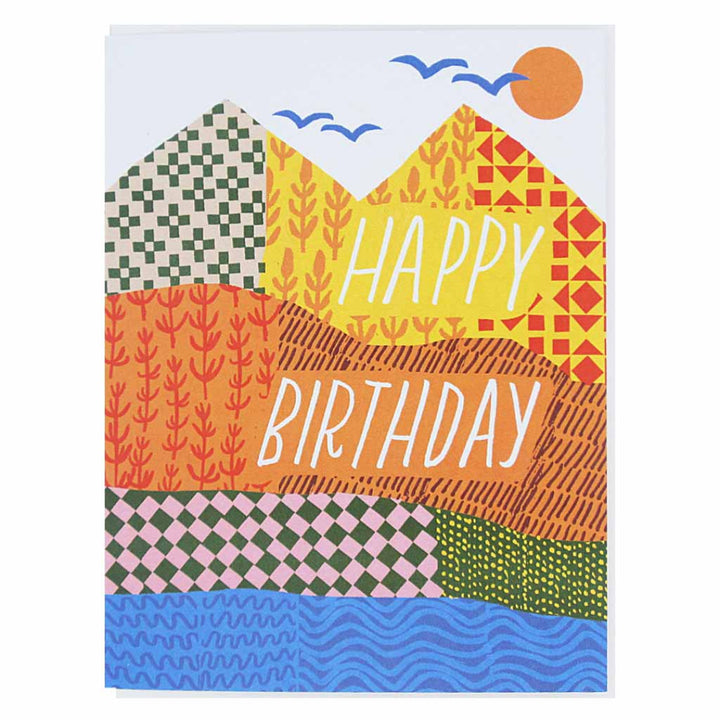 A colorful greeting card featuring a landscape design with mountains, a sun, birds, and a body of water. The mountains are depicted with various patterns and the words 