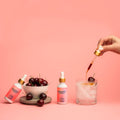 Hand pouring cherry syrup into a glass with ice and cherries, surrounded by Sibbion Soda products on a pink background.