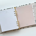 A white-coloured agenda with a black abstract design on the cover. The word "AGENDA" is printed in gold foil on the cover, along with the brand name "IDLEWILD CO." The agenda has a white elastic band to keep it closed.