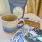 A handmade ceramic mug with a blue ombre glaze, featuring a speckled texture, displayed on a light gray background. The mug has a large, rounded handle and is made in Mississippi Mills, Ontario, Canada.