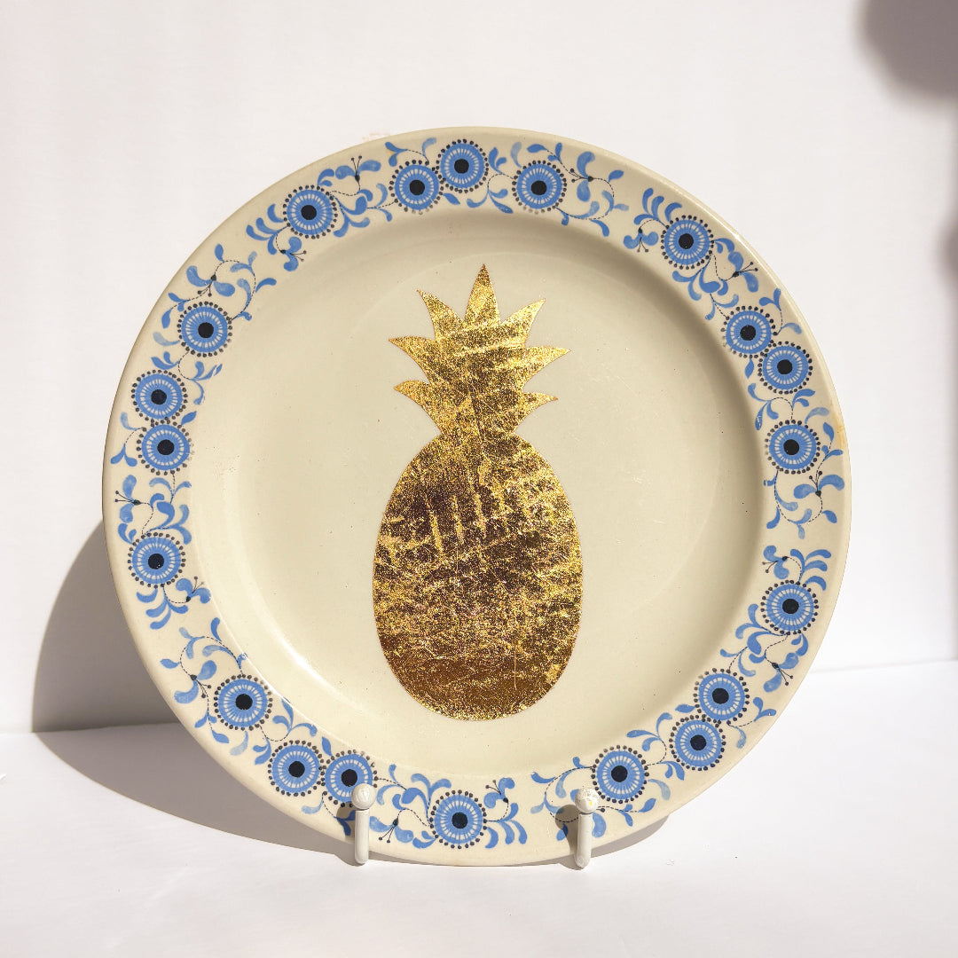 Decorative plate with gold pineapple and blue floral patterns on a white background
