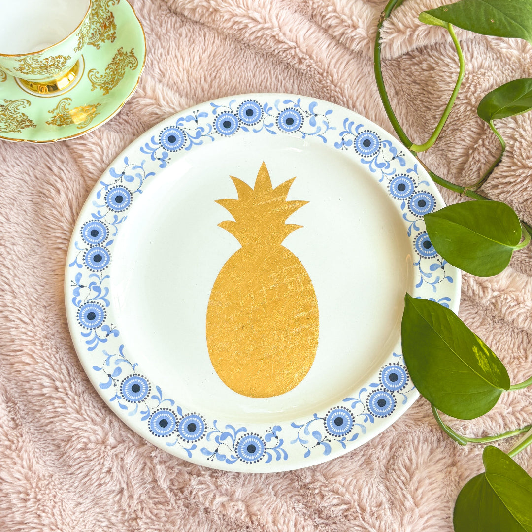 Decorative plate with a pineapple design on a textured surface with leaves.