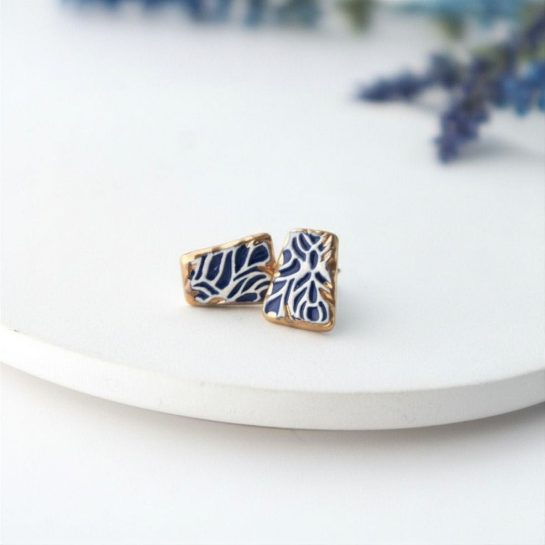 Pair of blue and gold earrings on a white plate with a blurred background