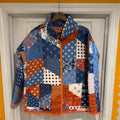 A quilted patchwork jacket hanging on a wooden hanger against a white paneled door, featuring a mix of blue, orange, and white patterned fabric panels.