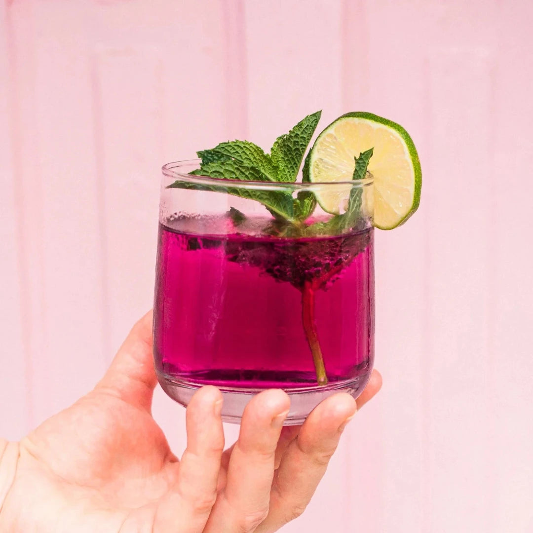 A glass jar filled with dried blueberries, mint leaves, and other ingredients. The jar has a white label with the Maiden Voyage logo and the product name "Blueberry Mint Cocktail Infusion."