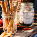 A glass jar filled with dried blueberries, mint leaves, and other ingredients. The jar has a white label with the Maiden Voyage logo and the product name "Blueberry Mint Cocktail Infusion."