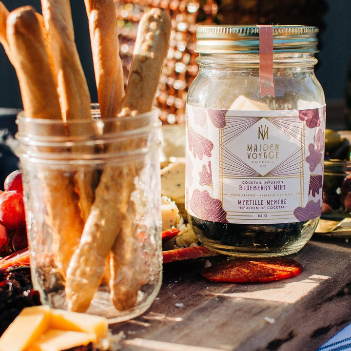 A glass jar filled with dried blueberries, mint leaves, and other ingredients. The jar has a white label with the Maiden Voyage logo and the product name 