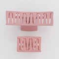 Two pink hair clips with a wavy design on a light gray background