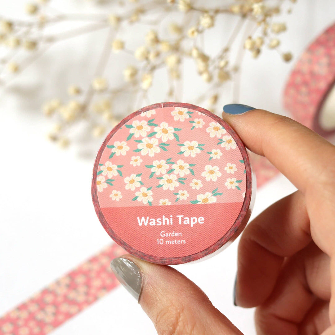Hand holding a roll of floral-patterned washi tape with additional tapes in the background.