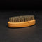 A brown, oval-shaped brush with a wooden handle and natural bristles. The brush is resting on a black surface.