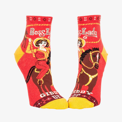 A pair of red ankle socks with yellow accents. One sock features a vintage-style illustration of a cowgirl riding a horse, with 