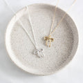 Two necklace pendants, one silver and one gold, on a speckled ceramic dish.