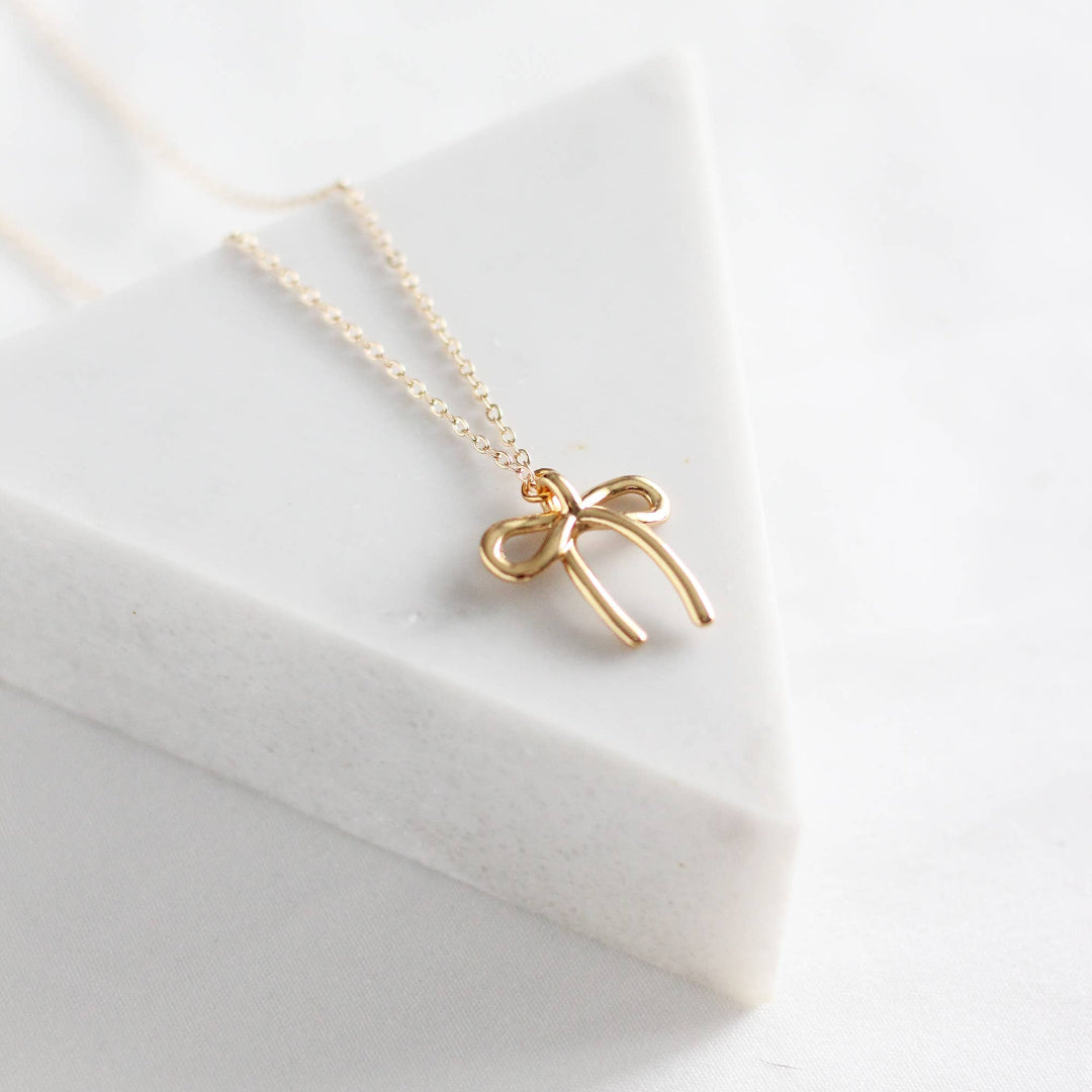 Gold bow-shaped necklace on a white surface
