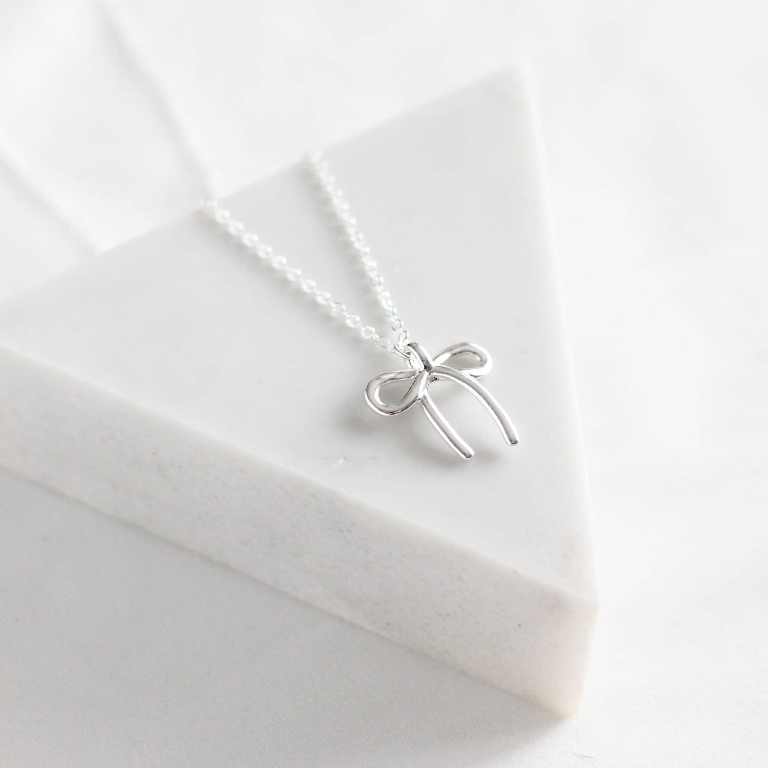Silver bow-shaped necklace on a white fabric background