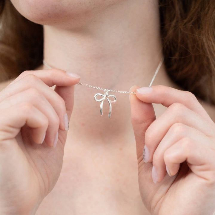 A silver plated necklace with a bow pendant.