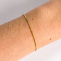 Gold bracelet on a wrist with a plain background