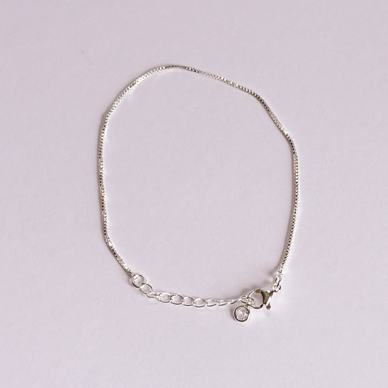 Silver bracelet with a small round charm on a light gray background