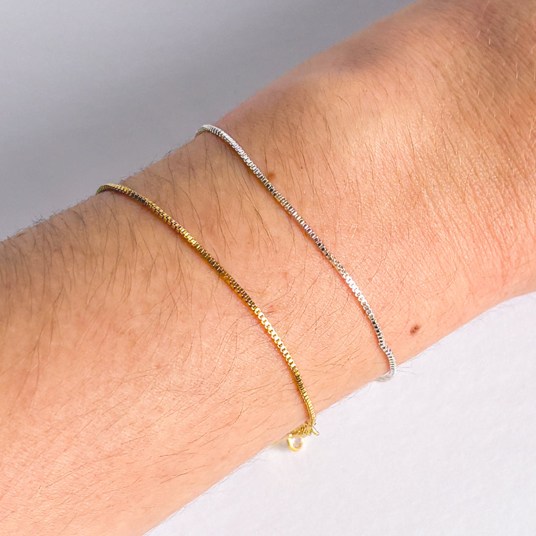 Two gold bracelets on a wrist against a neutral background