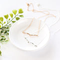 Two necklaces with branch pendants on a white surface. One necklace has a gold branch pendant, and the other has a silver branch pendant.
