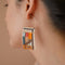 A pair of rectangular, tapestry-style earrings hand-stitched with small Japanese glass beads in a geometric pattern featuring shades of cream, orange, pink, light blue, teal, brown, and black. They hang from delicate, half-circle 14 KT gold filled wire hoops.