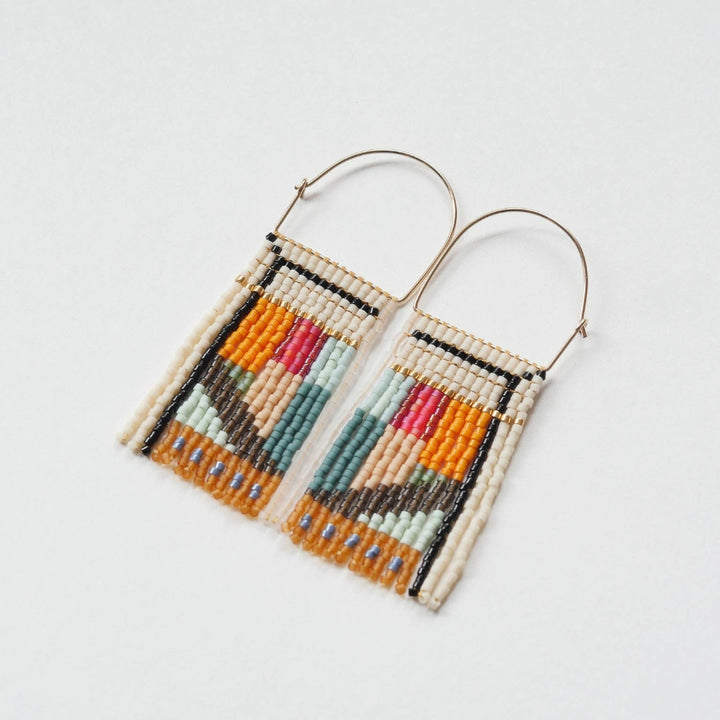 A pair of rectangular, tapestry-style earrings hand-stitched with small Japanese glass beads in a geometric pattern featuring shades of cream, orange, pink, light blue, teal, brown, and black. They hang from delicate, half-circle 14 KT gold filled wire hoops.