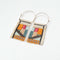 A pair of rectangular, tapestry-style earrings hand-stitched with small Japanese glass beads in a geometric pattern featuring shades of cream, orange, pink, light blue, teal, brown, and black. They hang from delicate, half-circle 14 KT gold filled wire hoops.