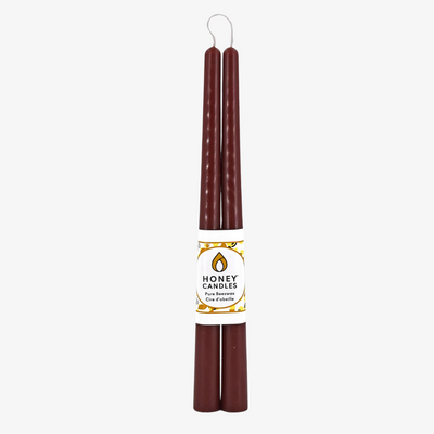 Two brown beeswax candles are standing upright, tied together with a string. The candles have a label that says 