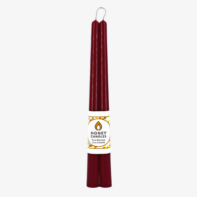 Two maroon beeswax candles are standing upright, tied together with a string. The candles have a label that says 