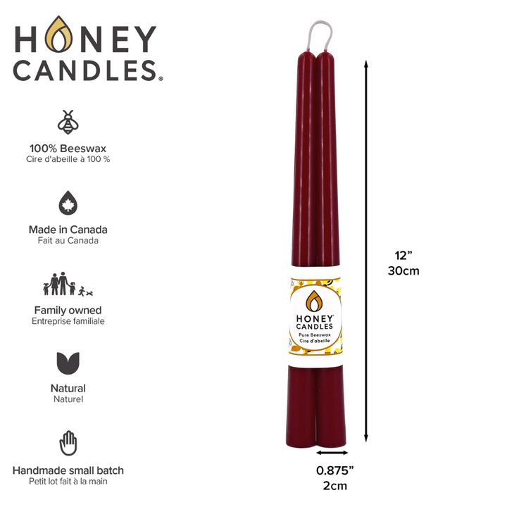 Two maroon beeswax candles are standing upright, tied together with a string. The candles have a label that says 