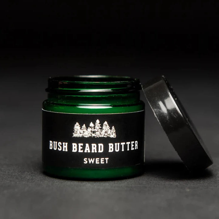 A dark green glass jar with a black lid. The jar is filled with beard butter and has a black label with the text 