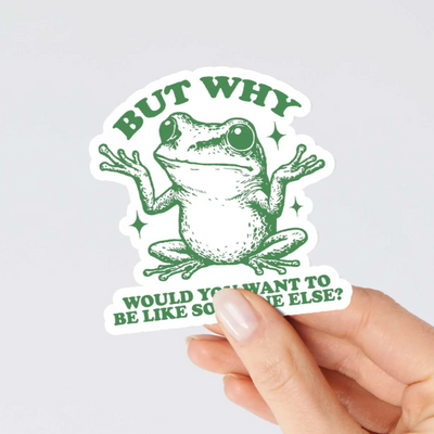 Sticker with a frog illustration and text held by a hand on a light gray background