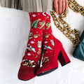 Red high-heeled shoes with festive pattern worn by a person, on a white surface.