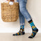 A pair of black socks with a laundry-themed design. The socks feature a washing machine, detergent bottles, a laundry basket, and socks themselves. It reads 