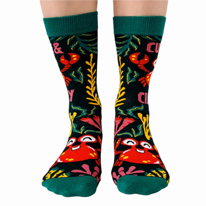 A pair of green socks with a crab-themed design. The socks feature a cute crab, a grumpy crab, and seaweed. The text 