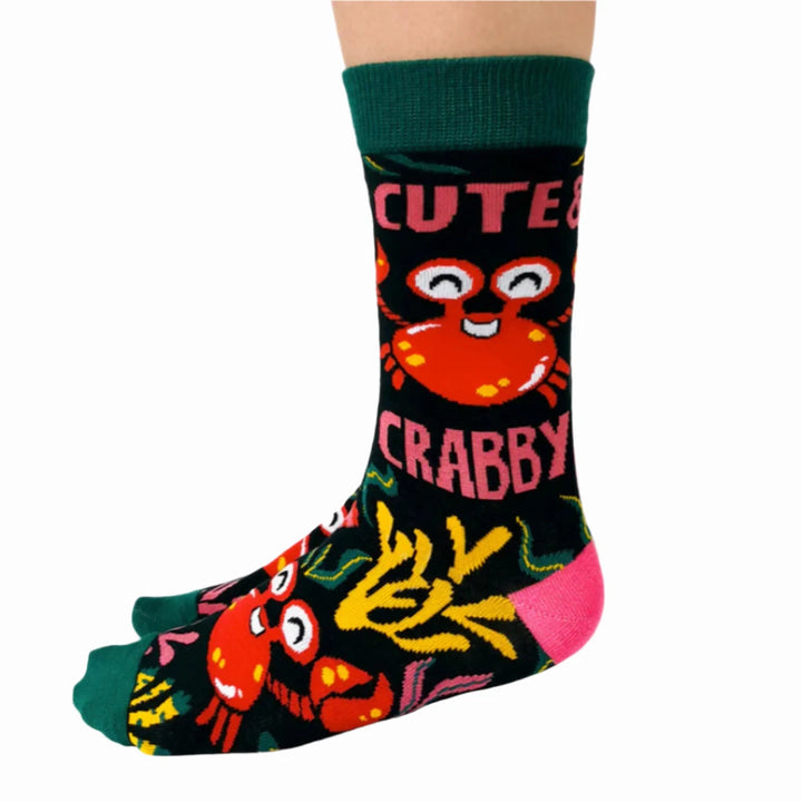 A pair of green socks with a crab-themed design. The socks feature a cute crab, a grumpy crab, and seaweed. The text 