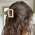 Brown hair with a gold hair clip against a neutral background