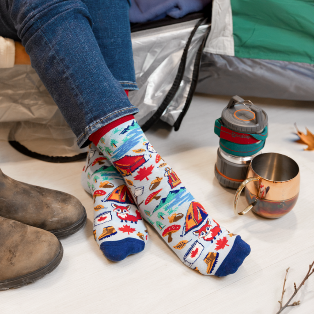 Person wearing colorful patterned socks sitting inside a tent with camping gear.