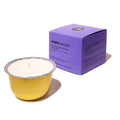 An amber glass candle with white wax sits in front of its purple packaging box on a clean white background. The box is labeled 'AMBER SMOKE' and features a small circular logo at the top.